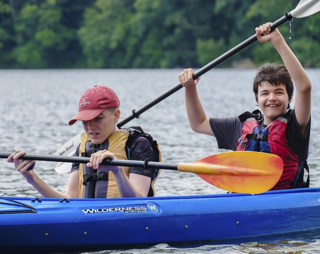 Two members in a kayak holding paddles and smiling